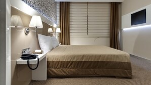 A hotel room with a large bed, two bedside lamps, a telephone, and a flat-screen TV mounted on the wall. - Sultan Hotel (Mersin)