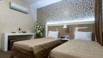A hotel room with two beds, a desk with a lamp, and a decorative wall.