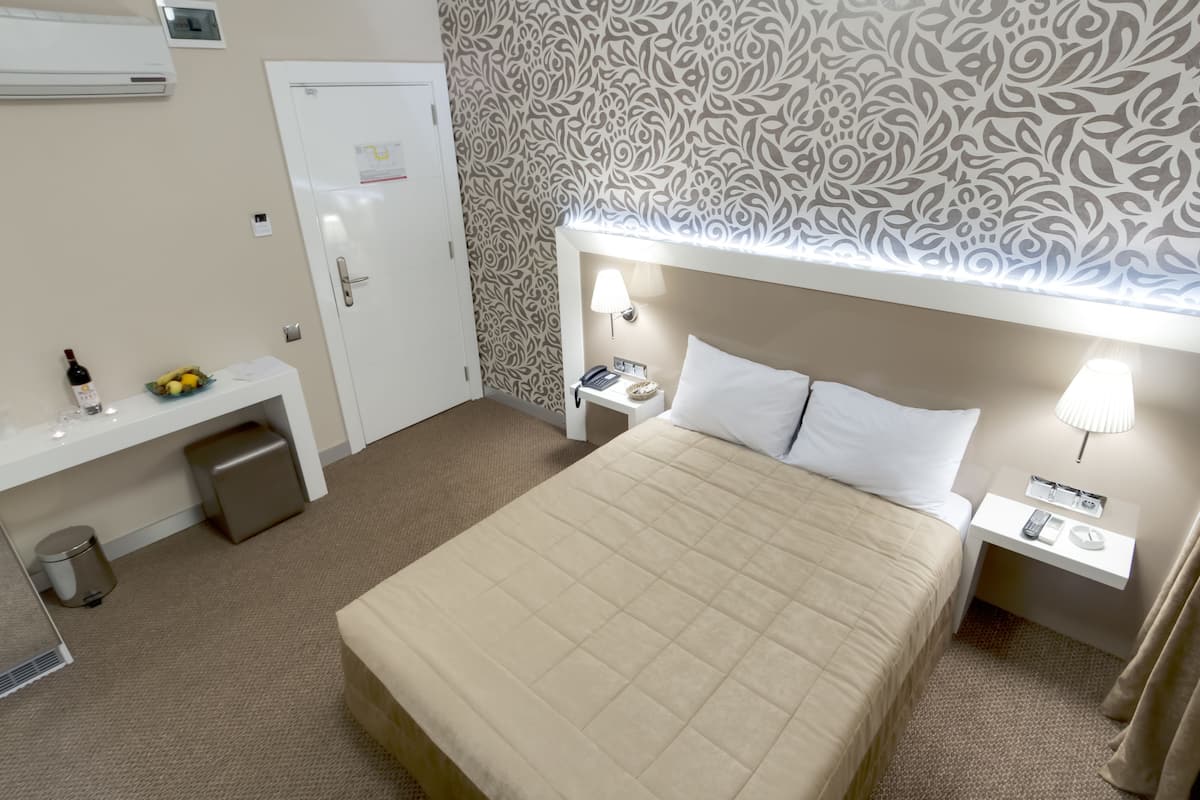 A hotel room with a bed, bedside tables, a desk, and a trash bin.