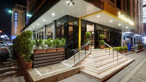 A modern hotel entrance with a glass facade, a staircase, and potted plants. - Sultan Hotel (Mersin)