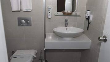 A small bathroom with a white sink, a mirror, a soap dispenser, and a towel rack.
