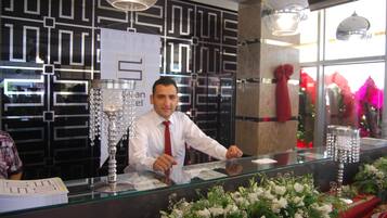 A reception desk with a glass partition, a decorative crystal vase, and a floral arrangement.