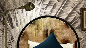 Una cama con cabecera de ratán, ropa de cama blanca y almohada azul.