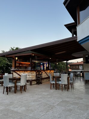 An outdoor bar area with stone walls, wooden tables, and chairs. There are bottles and glasses on the shelves, and a sign that reads "Erikli." - Olinda Hotel Agva (Sile)