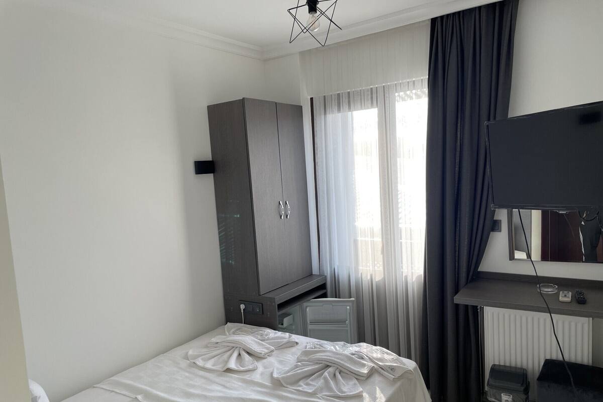 A hotel room with a bed, a wardrobe, a desk with a TV, and a radiator.