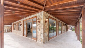 A covered outdoor area with stone walls and wooden beams, featuring large glass doors and windows, and a tiled floor. - Olinda Hotel Agva (Sile)