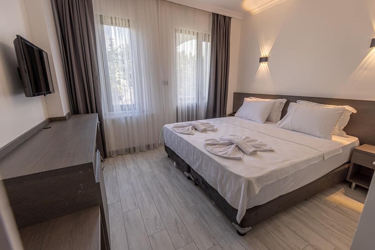 A hotel room with a bed, a TV, a desk, and a window with curtains.