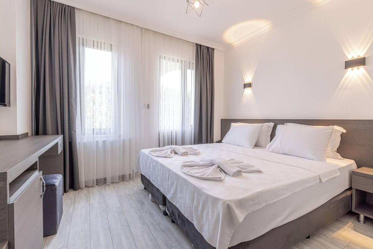 A hotel room with a bed, bedside tables, a desk, and a TV.