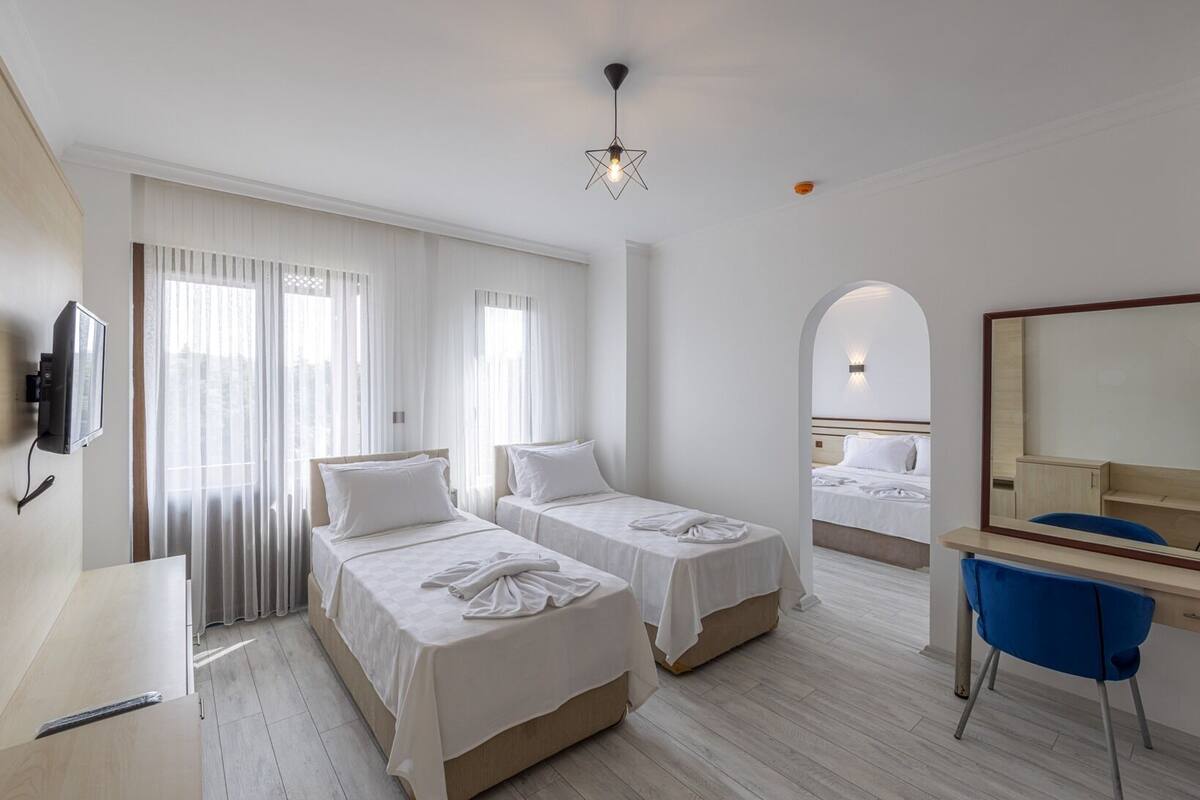 A hotel room with two beds, a desk, a chair, a TV, and a large mirror.