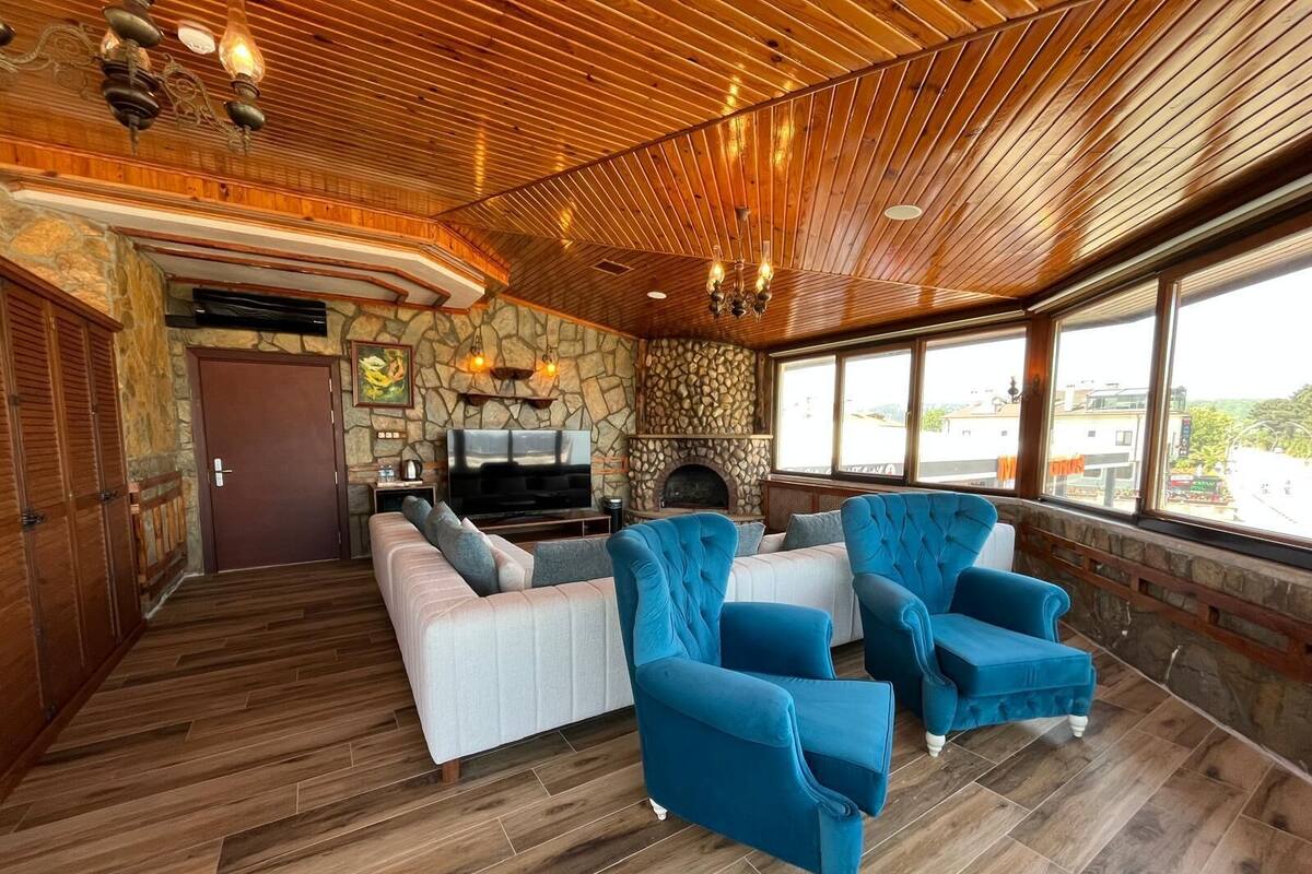 A spacious living area with a stone fireplace, wooden ceiling, and large windows.