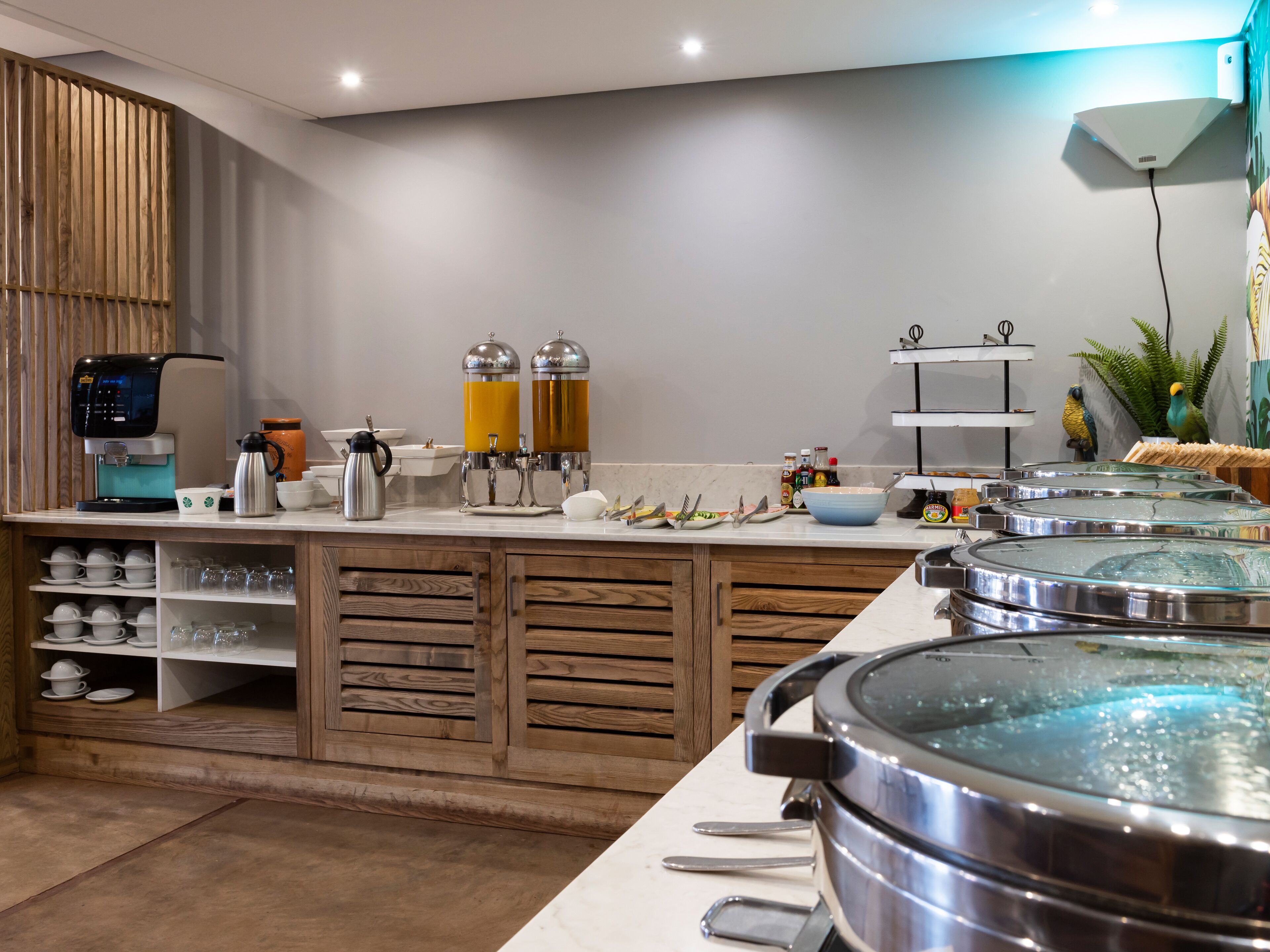A modern kitchen with a coffee machine, two orange juice dispensers, and a variety of utensils and dishes on the counter.