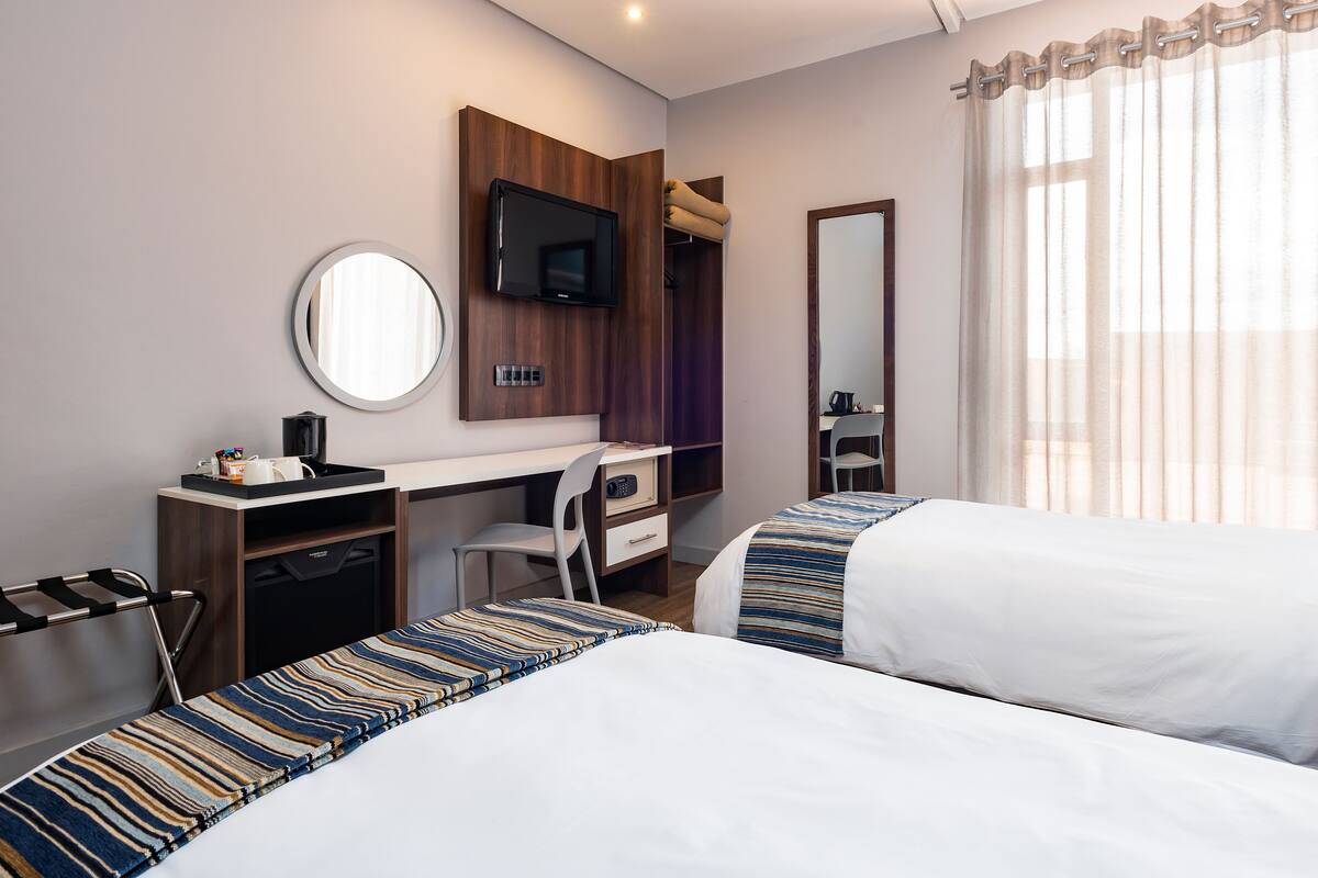 A hotel room with a bed, a desk, a chair, a TV, and a mirror.