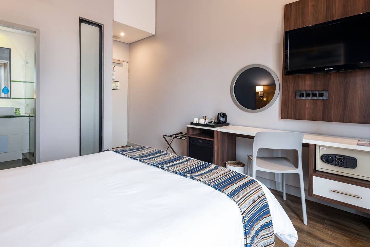 A hotel room with a bed, a desk, a chair, a TV, and a mirror.
