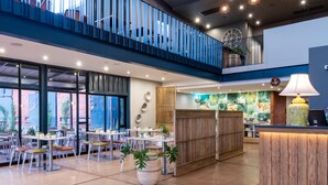 A spacious indoor area with multiple tables and chairs, a reception desk, and a balcony with railings. - Urban Hotel Kathu (Kathu)