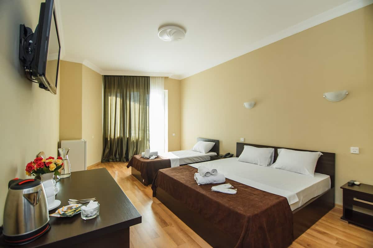 A hotel room with two beds, a desk with a coffee maker, a TV mounted on the wall, and a window with curtains.