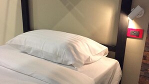 A neatly made bed with white linens in a room with a brick wall and a modern light fixture. - Picoco hostel (Koh Samui)