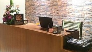 A reception desk with a brick wall backdrop, a clock, and a small plant. - Picoco hostel (Koh Samui)