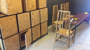 A room with a table and chairs, a stack of wooden boxes, and a dark wall. - Picoco hostel (Koh Samui)