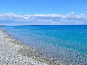 Ein Strand mit Kieselsteinen und ruhigem, blauem Wasser unter einem strahlend blauen Himmel.