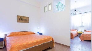 A hotel room with a large bed, a desk, and a chair. There are two windows and a door leading to another room. - B&B Shalom (Condofuri)