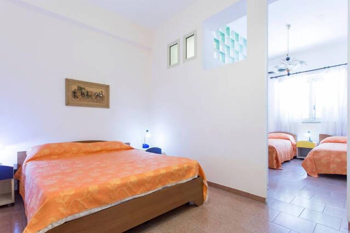 A hotel room with a large bed, a desk, and a chair. There are two windows and a door leading to another room.
