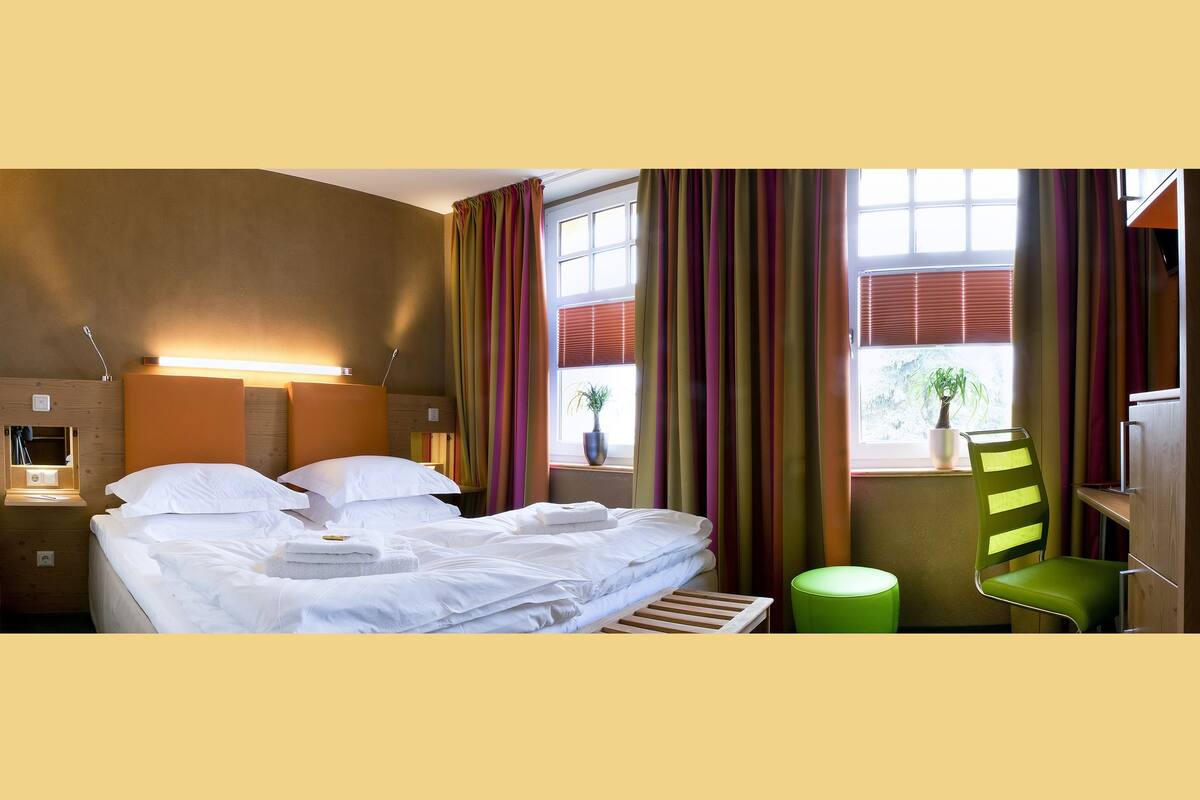 Ein Hotelzimmer mit einem Bett, Nachttischen, einem Sessel und einem Fenster mit Vorhängen.