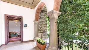 A hallway with a stone archway, a wooden door, and a potted plant with white flowers. - Ramé Suites (Bergamo)