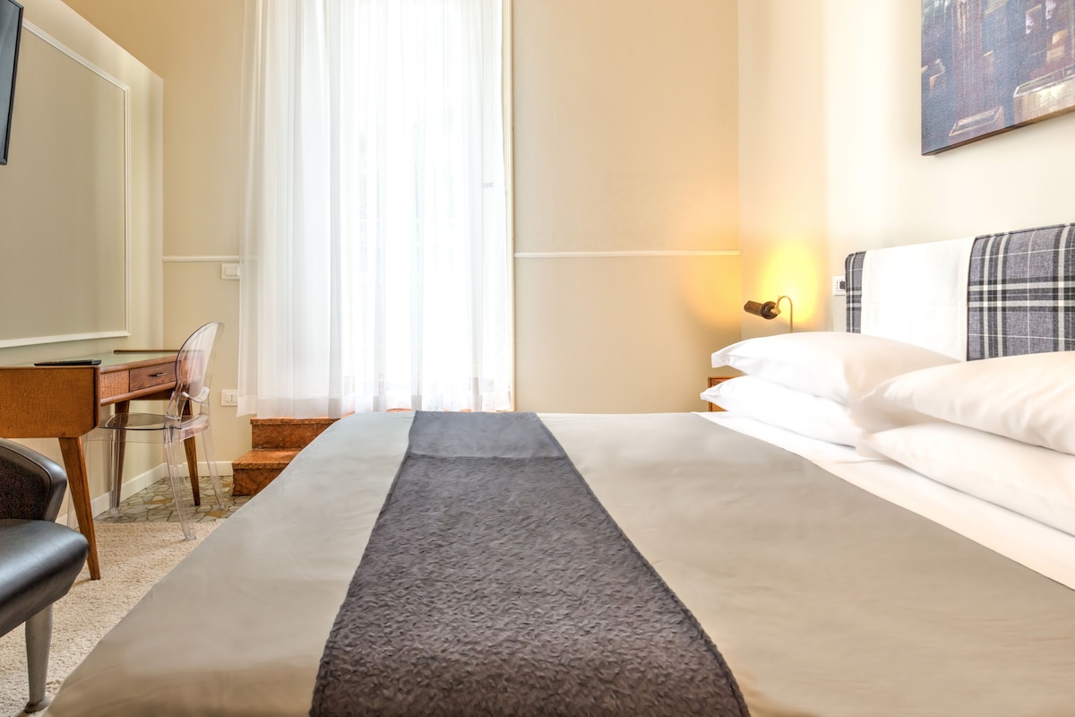 A hotel room with a bed, a desk, a chair, and a TV.