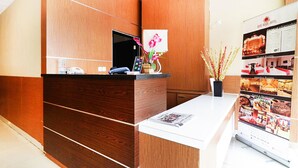 A hotel reception desk with a wooden finish, a digital display, and a floral arrangement. - Quds Express Hotel (Jakarta)