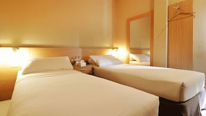 A hotel room with two single beds, a nightstand with toiletries, a mirror, and a wooden wardrobe. - Quds Express Hotel (Jakarta)