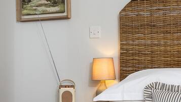 A neatly arranged bedroom with a bed, a bedside table with a lamp, a radio, and a framed painting on the wall.