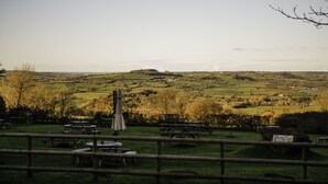 A rural landscape with picnic tables and a stone building, likely a restaurant or inn, in the foreground. - Winyard's Gap Inn (Beaminster)