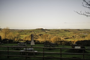 A rural landscape with picnic tables and a stone building, likely a restaurant or inn, in the foreground.