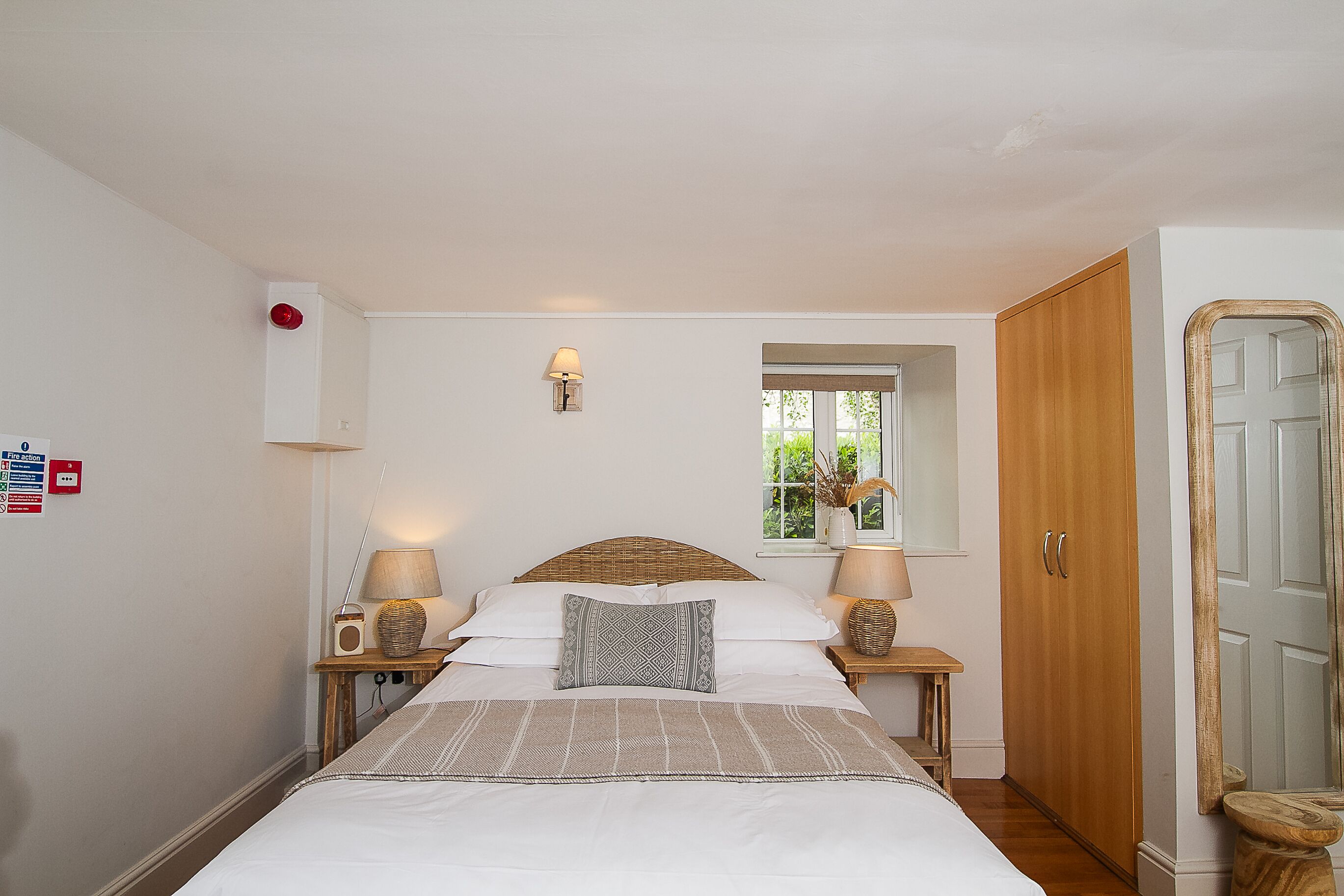 A neatly arranged bedroom with a large bed, two bedside tables with lamps, a window with a view, and a wardrobe.