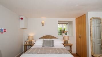 A neatly arranged bedroom with a large bed, two bedside tables with lamps, a window with a view, and a wardrobe.
