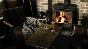 A cozy room with a brick fireplace, leather chairs, and a wooden table with a glass of beer. - Winyard's Gap Inn (Beaminster)