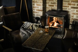 A cozy room with a brick fireplace, leather chairs, and a wooden table with a glass of beer.