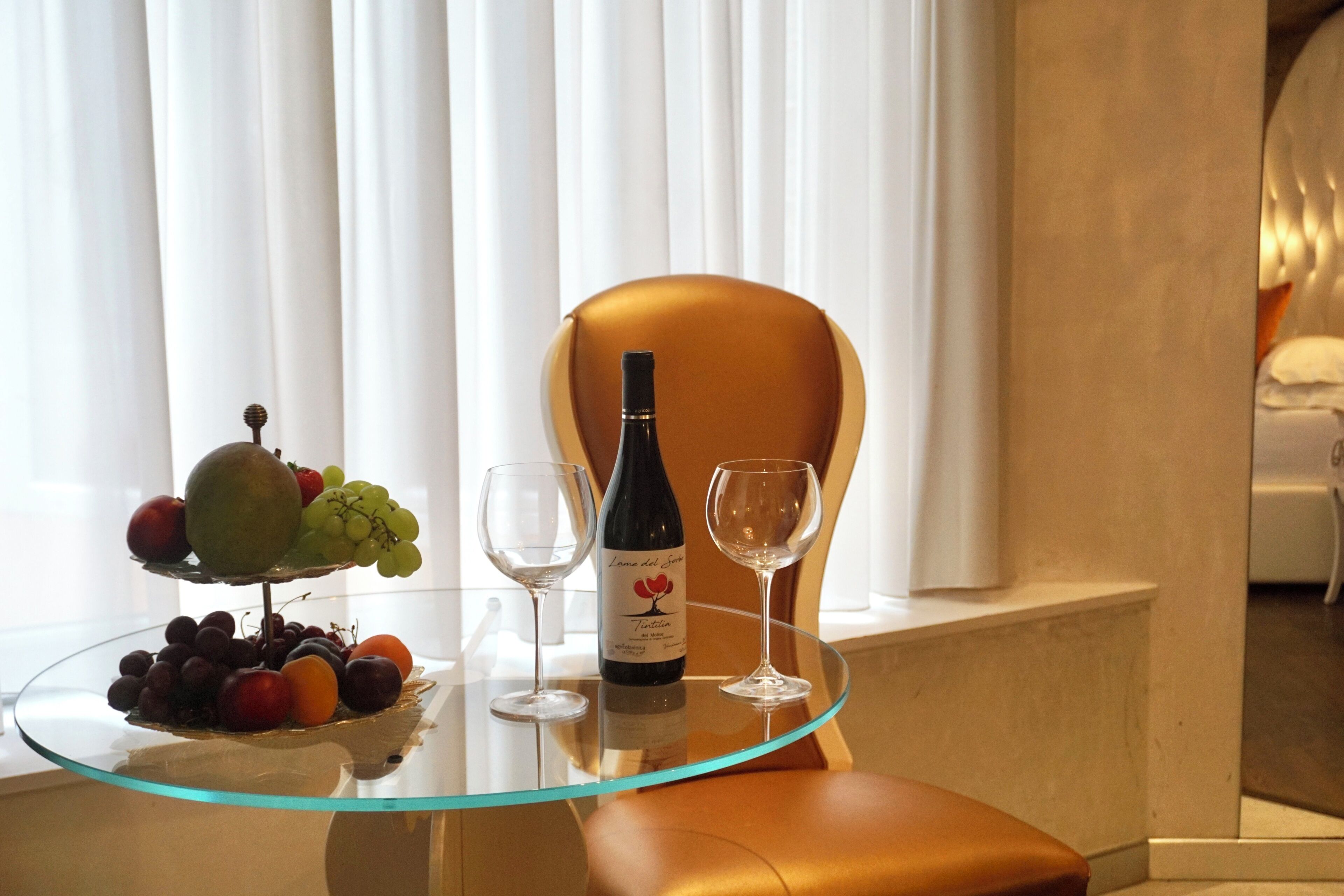 A glass table with a bottle of wine, two wine glasses, and a fruit platter.