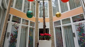 A multi-level atrium with large windows, decorative red and green ornaments, and potted red flowers. - Hotel Vespasiano (Rome)