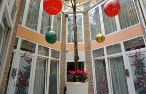A multi-level atrium with large windows, decorative red and green ornaments, and potted red flowers. - Hotel Vespasiano (Rome)