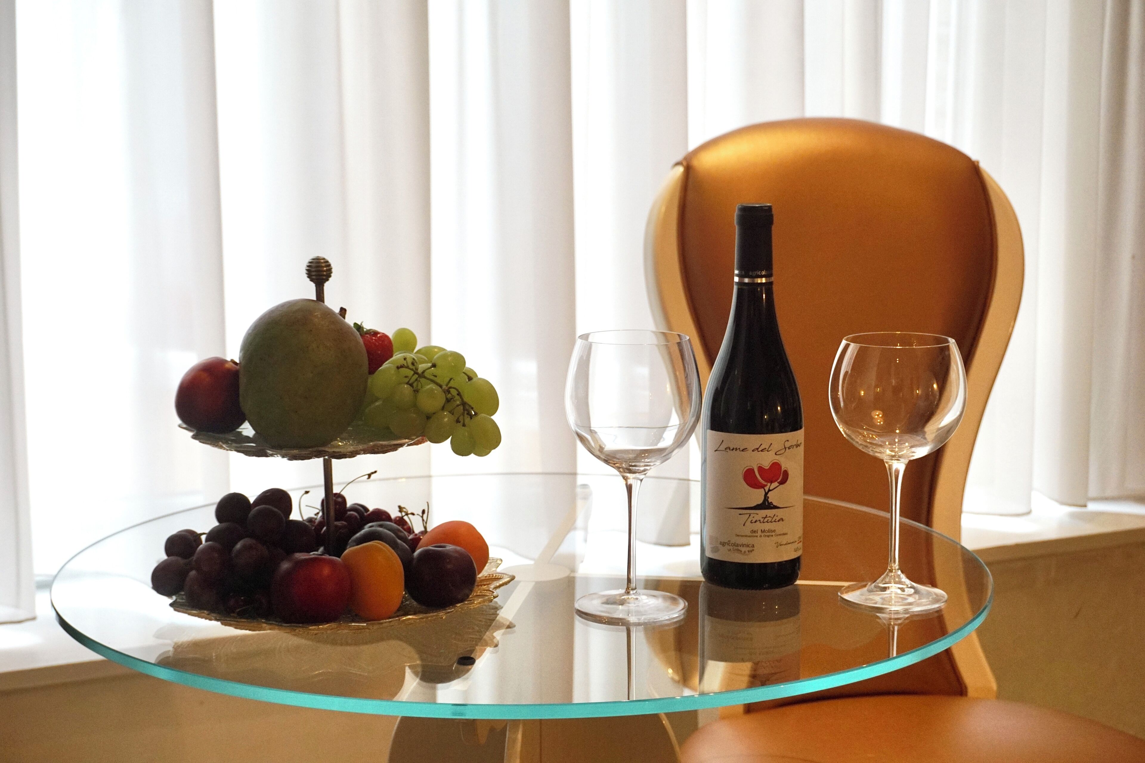 A glass table with a bottle of wine, two wine glasses, and a fruit platter.