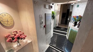A modern hotel lobby with a reception desk, a clock, and a staircase. - Hotel Vespasiano (Rome)