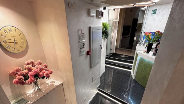 A modern hotel lobby with a reception desk, a clock, and a staircase. - Hotel Vespasiano (Rome)