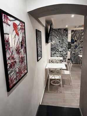 A modern interior with a dining area featuring white tables and chairs, framed artwork on the walls, and a patterned wallpaper design. - Hotel Vespasiano (Rome)