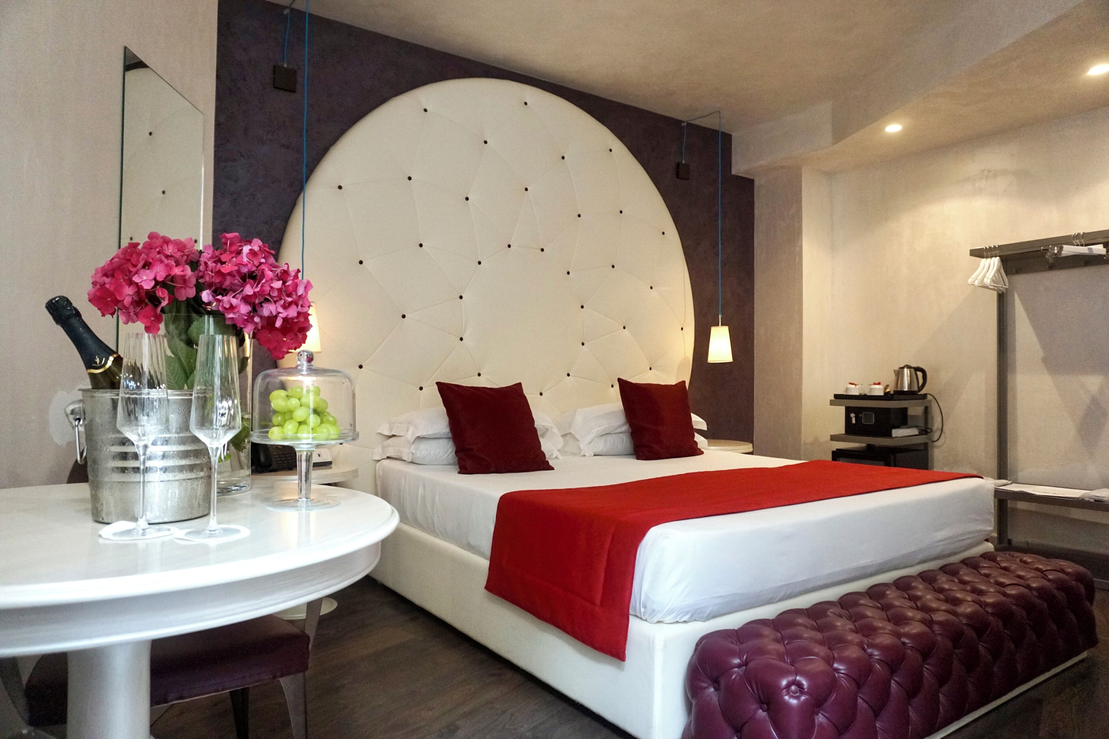 Ein Hotelzimmer mit einem großen Bett, einem runden Tisch mit Blumenvase, einer Kaffeemaschine und einer roten Bank.