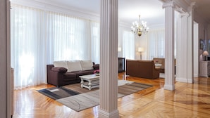 A spacious living room with a wooden floor, a brown sofa, a white coffee table, and a chandelier. - Hotel Mediodia (Madrid)