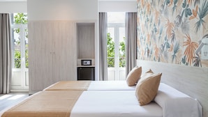 A hotel room with a large bed, a small desk, and a view of greenery outside. - Hotel Mediodia (Madrid)