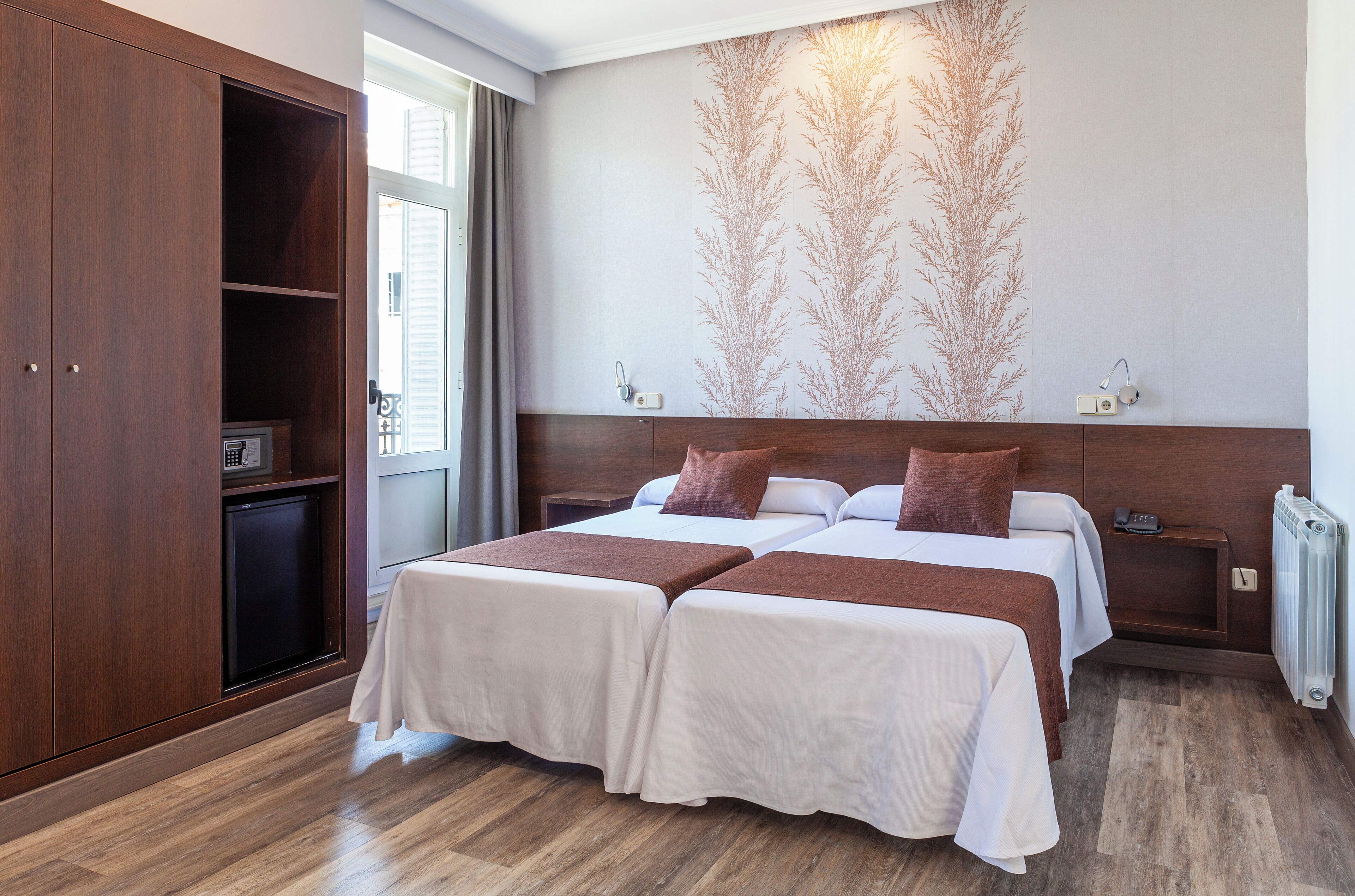 Habitación de hotel con dos camas, un armario, un escritorio y un radiador.