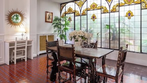 A dining area with a wooden table and chairs, a large stained glass window, and a sunburst mirror on the wall. - Hotel Mediodia (Madrid)
