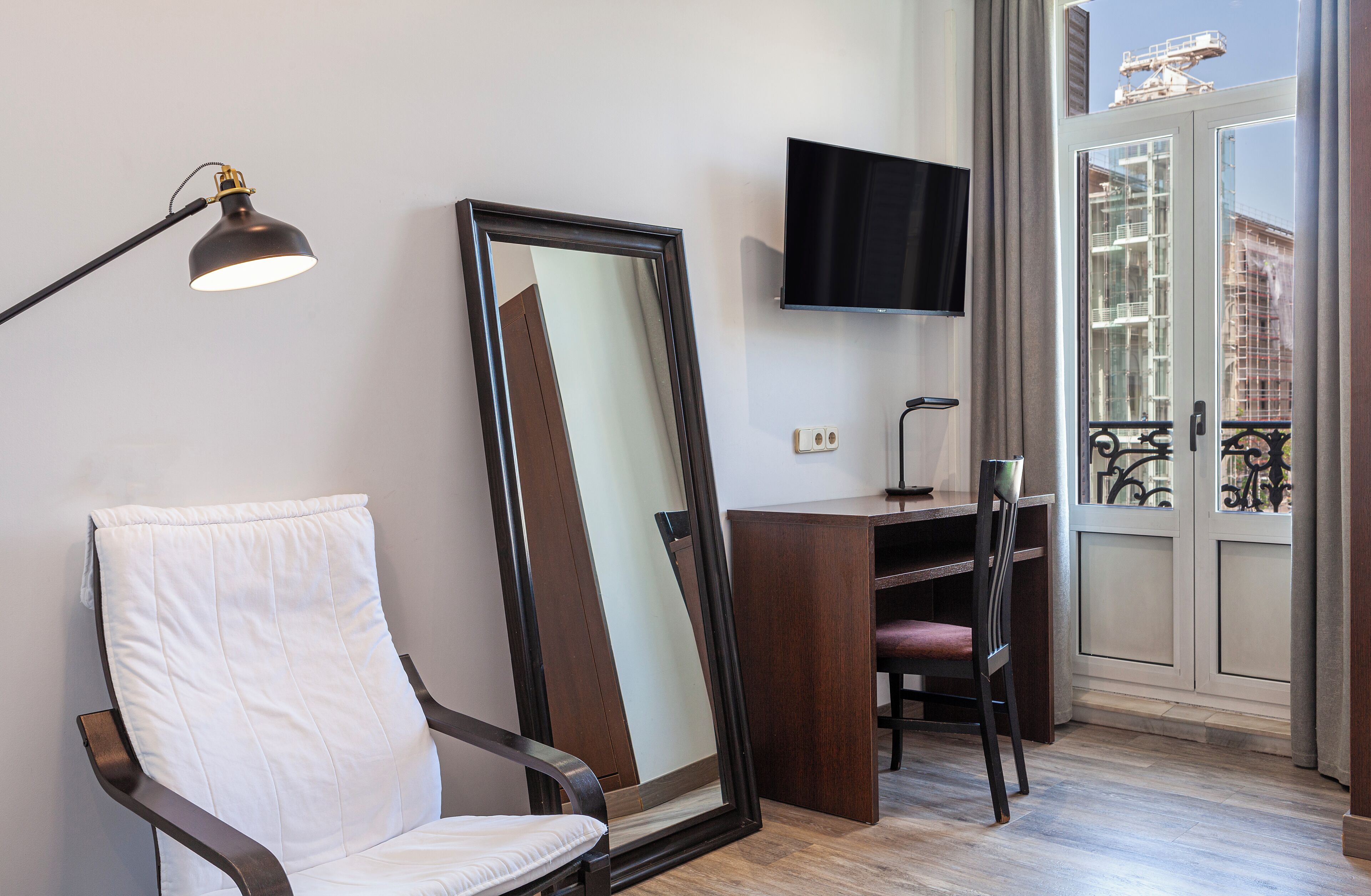 A room with a white chair, a desk, a television, and a large mirror.